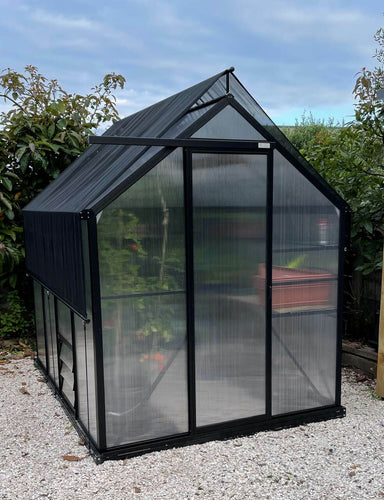2m x 2.6m polycarbonate greenhouse shown in a garden sitting on white pebbles with shade cover accessory on top.