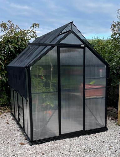 2m x 2.6m polycarbonate greenhouse shown in a garden sitting on white pebbles with shade cover accessory on top. 